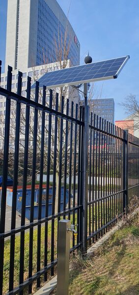Solarpanel auf Zaun, im Hintergrund großes Gebäude