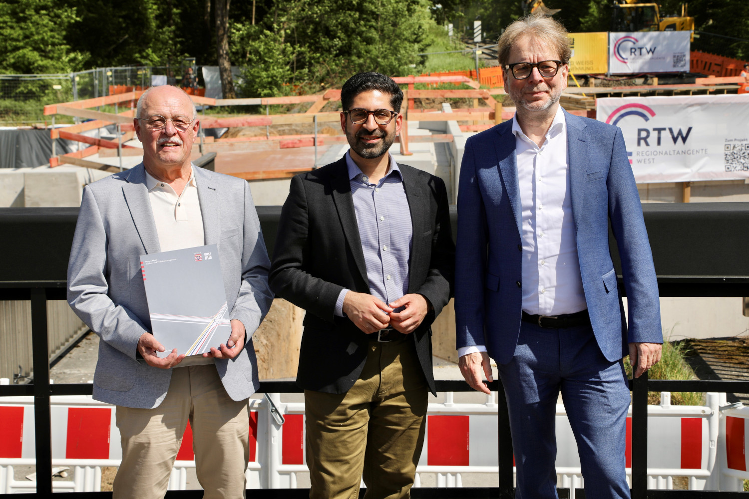 von rechts nach links stehen Horst Amann, Kaweh Mansoori und Wolfgang Siefert nebeneinander, Horst Amann hält den Förderbescheid in den Händen