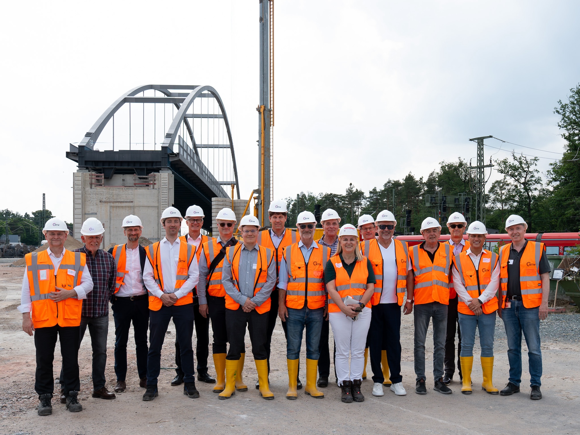 Gruppenbild von Menschen mit Warnwesten und Bauhelmen, im Hintergrund die Stabbogenbrücke